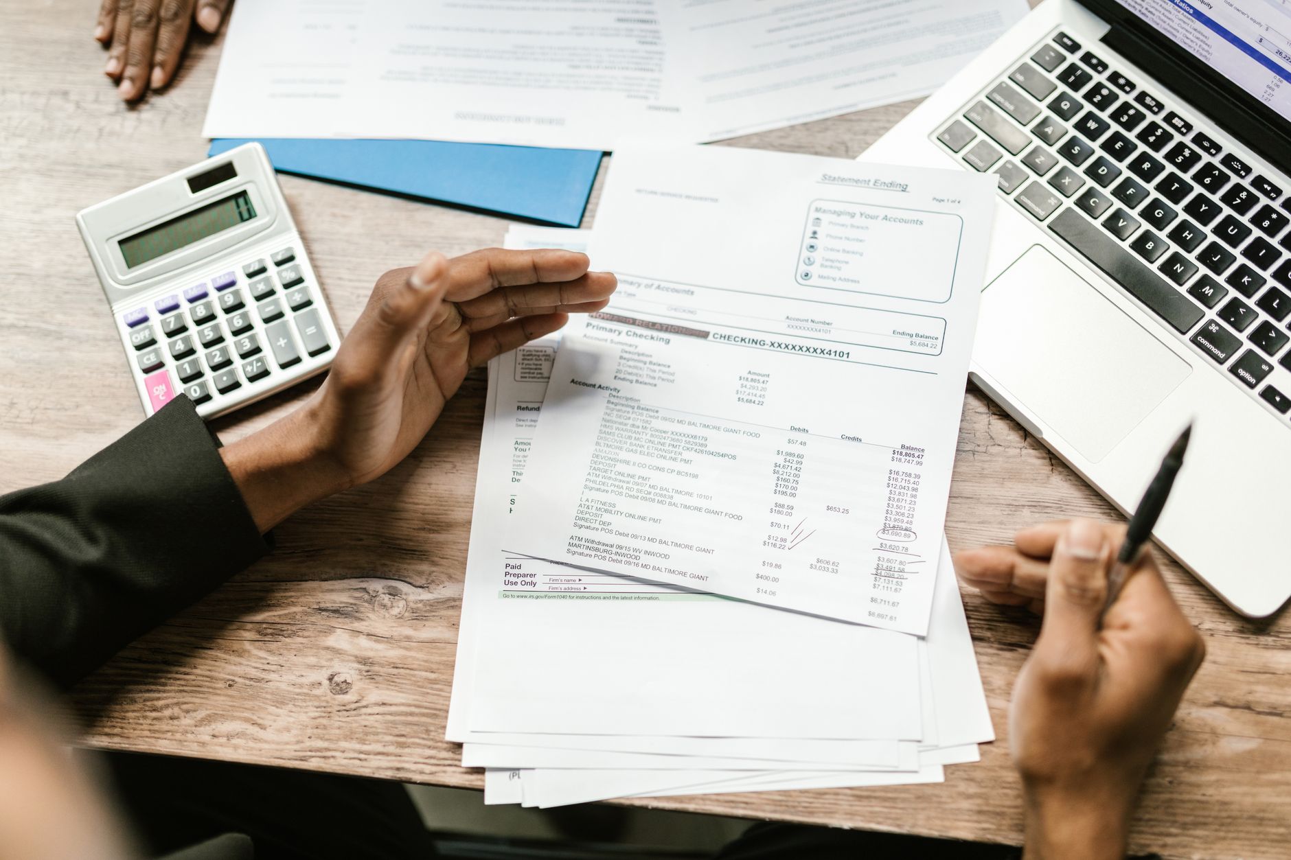 A person reviewing an expense report on a laptop with paper receipts and a calculator on the desk.