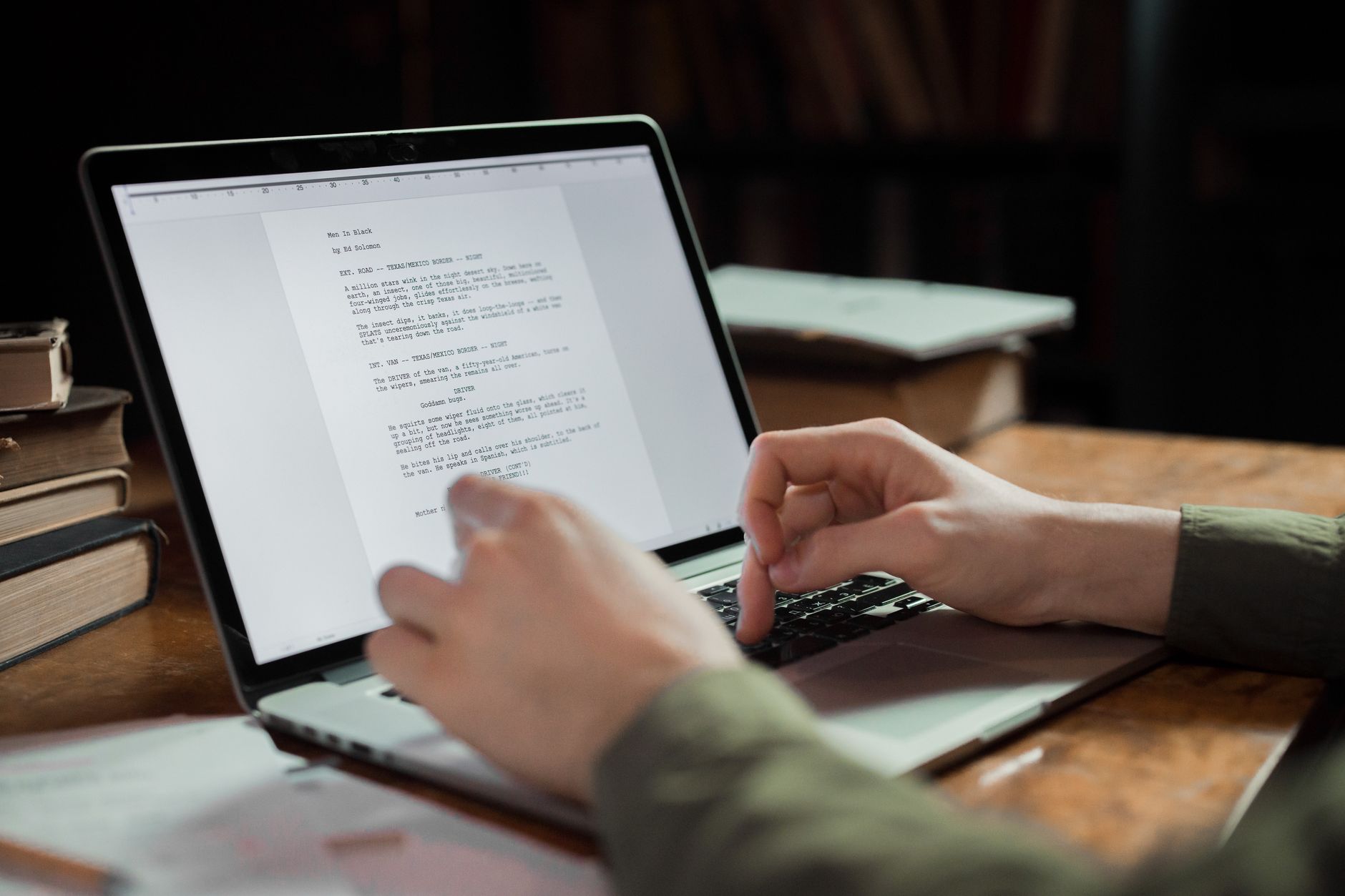 Writer typing on a laptop at a desk lit by a warm lamp